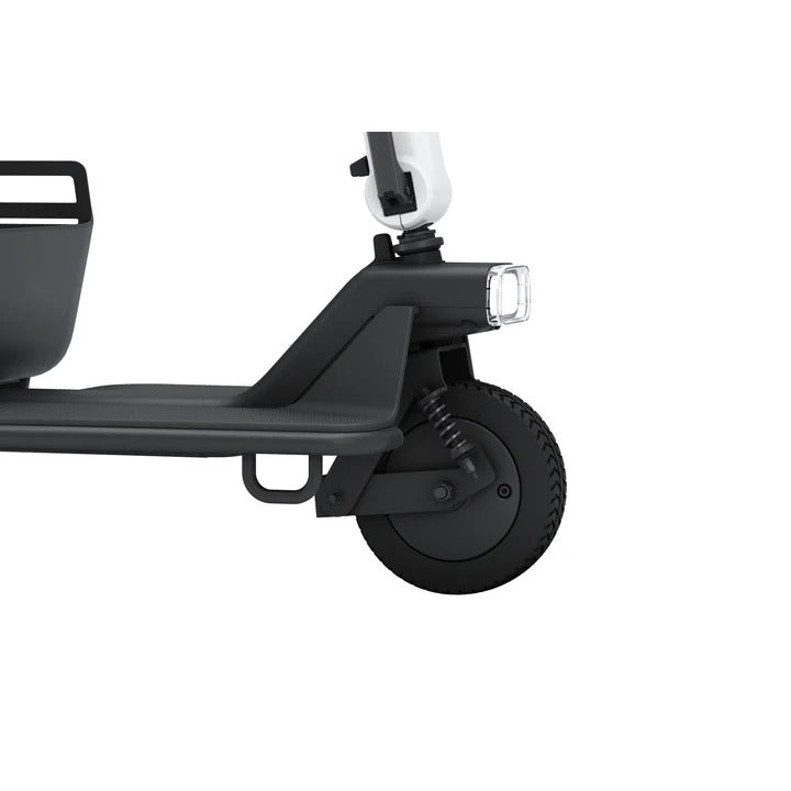 Nahaufnahme des WHILL Model R 3-Rad von Whill: zeigt das schwarze Vorderrad, die Federung, den Scheinwerfer, einen Teil des vorderen Korbes und die Plattform. Der wendige Mobilitätsroller ist vor einem weißen Hintergrund zu sehen.