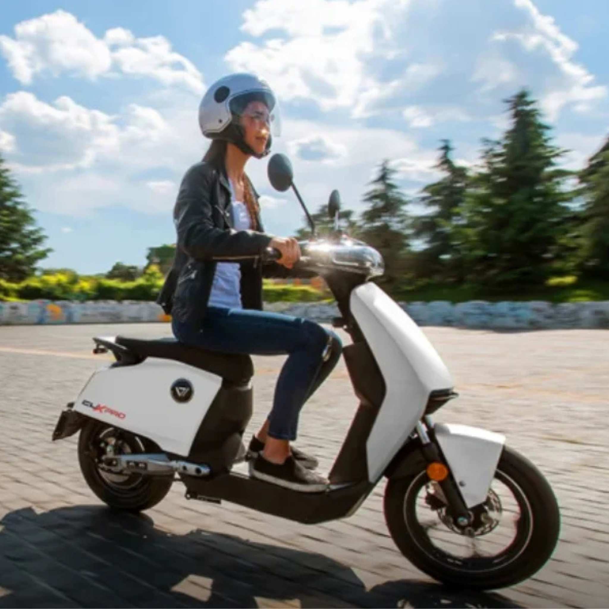 Ein Fahrer mit Helm und Sonnenbrille cruist auf einem weißen Super Soco Elektroroller CUx Pro, dem leichten 45 km/h E-Scooter mit Bosch-Power, an einem sonnigen Tag zwischen Bäumen und blauem Himmel.