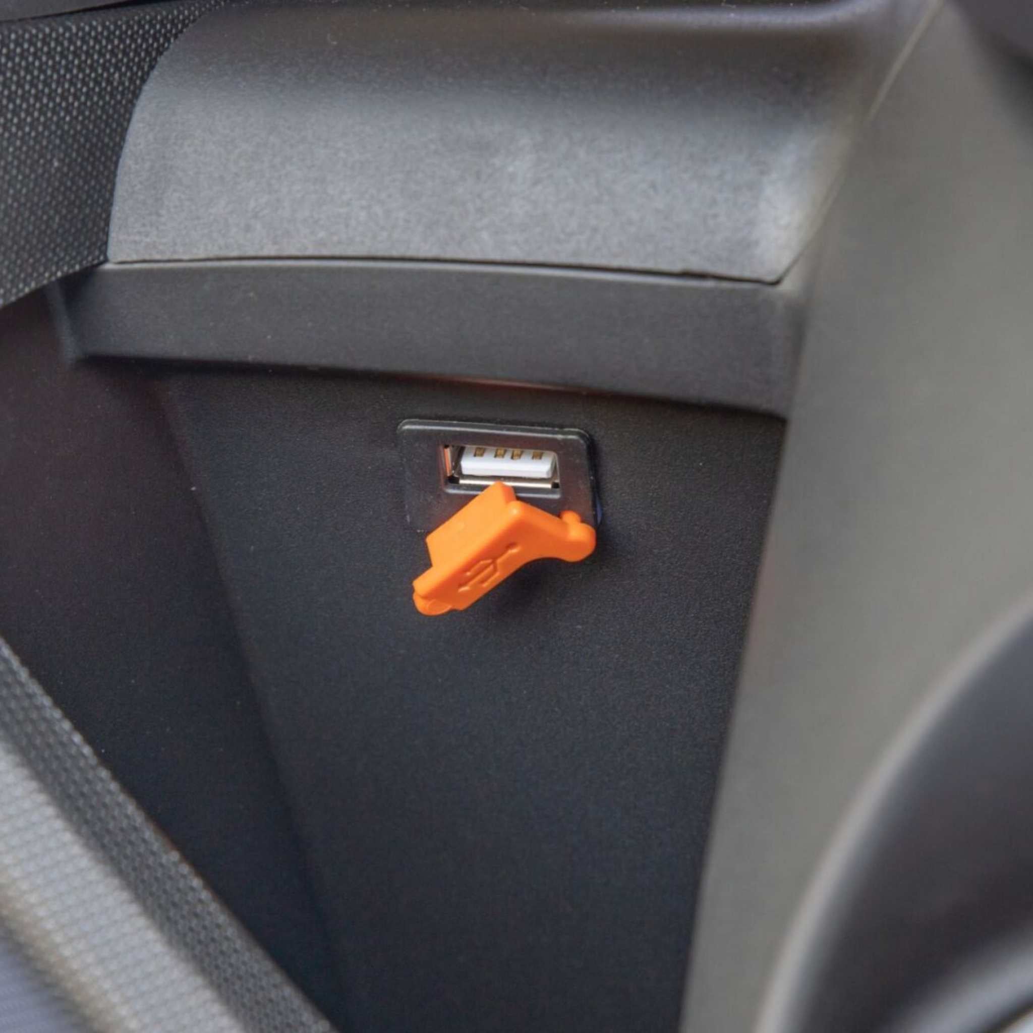 Eine Nahaufnahme eines USB-Anschlusses mit einer orangefarbenen Abdeckung, die auf einer schwarzen Platte im Inneren des Trinity Jupiter GT 300 Elektroroller & E-Scooter von Trinity angebracht ist. Er erreicht 120 km/h und bietet eine Reichweite von 300 km.