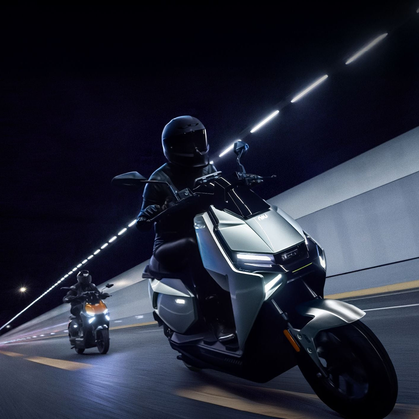 Zwei Personen fahren mit dem NIU FQiX 300 Elektroroller 80 km/h mit 3600W Motor und Dual-Akku durch einen gut beleuchteten Tunnel bei Nacht, beide mit schwarzen Helmen und dunkler Kleidung. Der Lead-Scooter leuchtet mit seinem hellen LED-Scheinwerfer und dem futuristischen NIU-Design.
