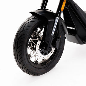 Nahaufnahme des schwarzen Vorderrads des Coopop Bobber mit Scheibenbremse und Speichenfelge vor weißem Hintergrund – ein Blick auf Coopops stärksten E-Chopper seiner Klasse (45 km/h, L1e), geräuschlos und leistungsstark.
