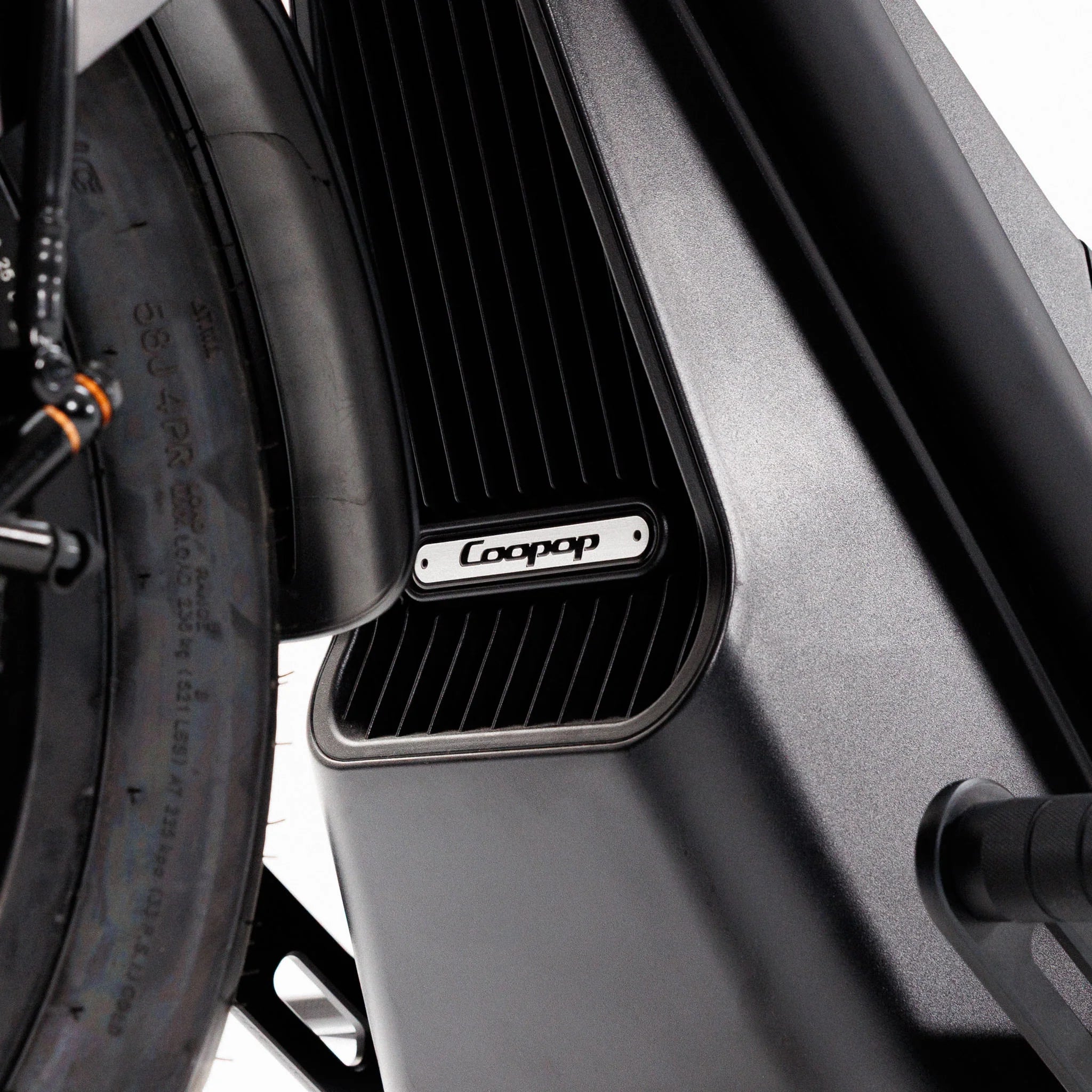 Nahaufnahme des Rahmens des Coopop Bobber E-Chopper, auf der ein Teil des Hinterreifens und ein Metalltypenschild mit dem Coopop-Logo zu sehen sind – die das markante Design und den leistungsstarken 45 km/h-Elektroantrieb unterstreichen.
