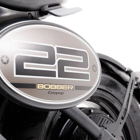 Nahaufnahme des Hinterrads und des Kotflügels des Coopop Bobber mit einem ovalen 22er-Kennzeichen sowie den Aufdrucken „BOBBER“ und „Coopop“. Das Reifenprofil und der Rahmen des E-Choppers unterstreichen den geräuschlosen, leistungsstarken Elektroantrieb mit 45 km/h (L1e).
