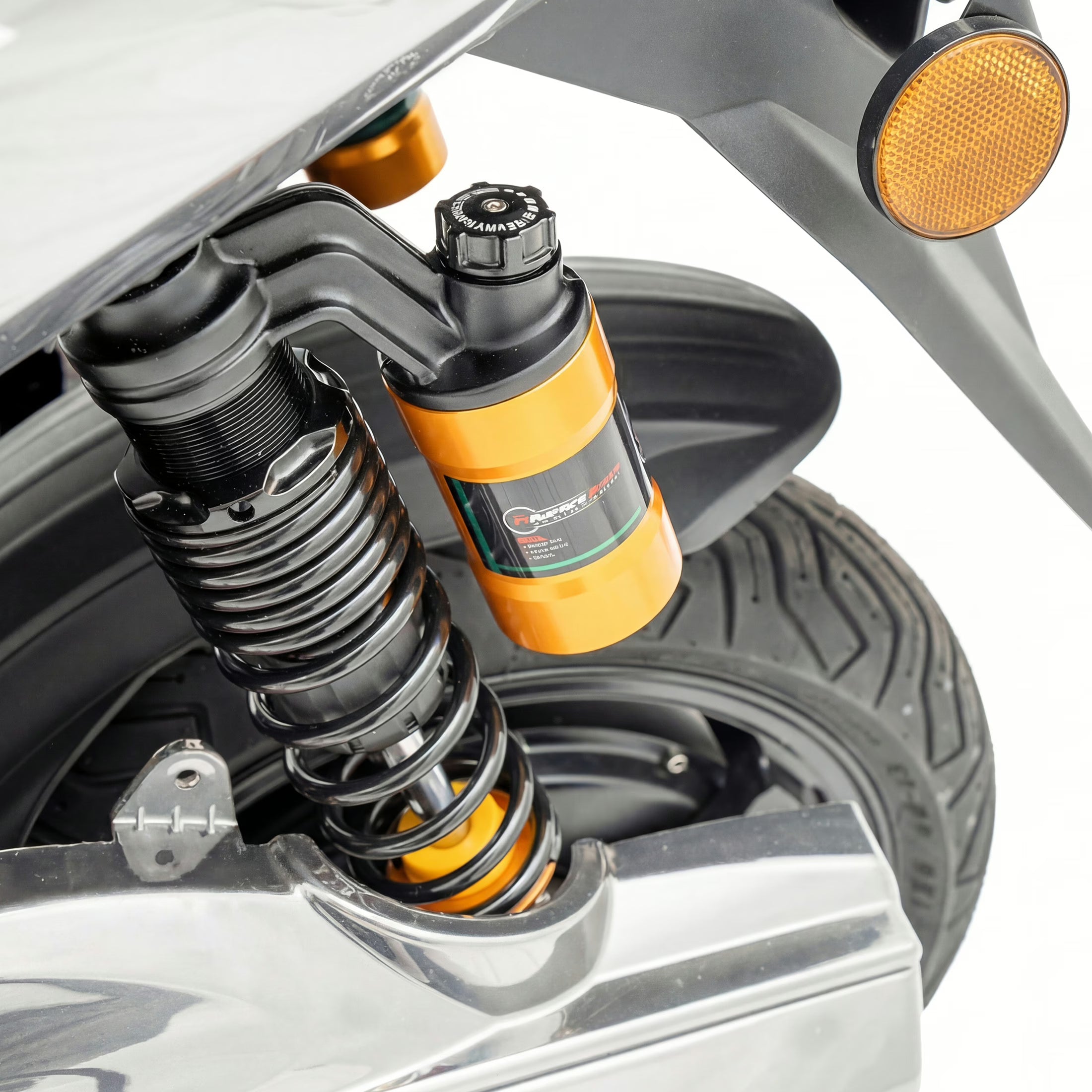Nahaufnahme der Hinterradaufhängung des Elektrorollers „Trinity Jupiter GT 300“ mit einer schwarzen Schraubenfeder und einem goldfarbenen Stoßdämpfer in der Nähe des Hinterrads; ein Teil des reflektierenden Kotflügels ist zu sehen. Marke: Trinity. Modell 2026.