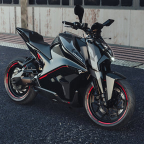 Ein auffälliges Ultraviolette F77 Superstreet Recon - Sportliches Elektromotorrad steht auf dunklem Asphalt vor einem verwitterten Gebäude, seine schwarz-silberne Karosserie mit roten Akzenten zieht die Blicke auf sich - bereit für die Straßen der Stadt.