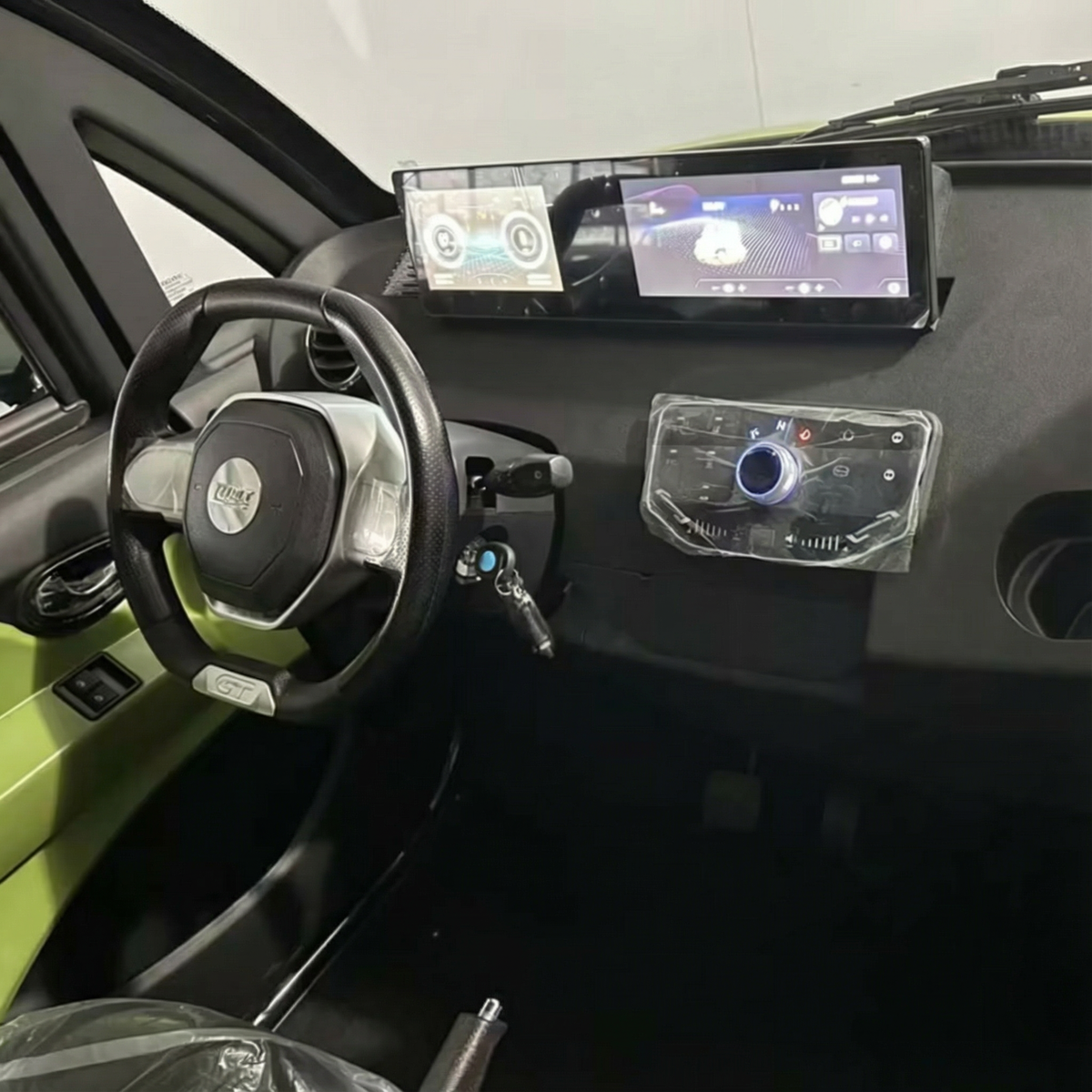 Das elegante Armaturenbrett des City Twister Luqi EV300 Pro Kabinenrollers (Modell 2026) verfügt über zwei digitale Bildschirme, ein Lenkrad mit verdeckten Bedienelementen und einen in die Zündung eingesteckten Schlüssel. Der Innenraum des Elektro-Miniautos ist in stilvollem Schwarz und Grün gehalten.