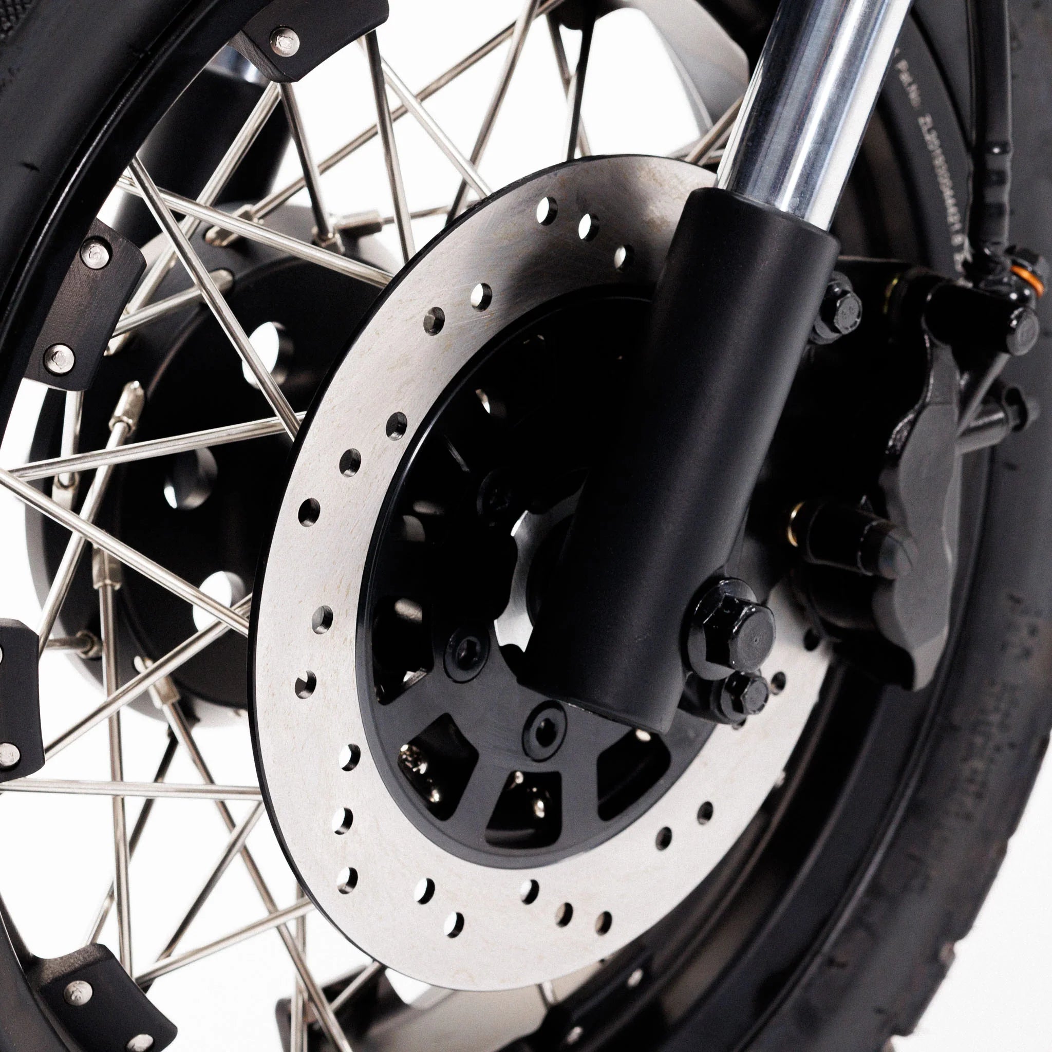 Nahaufnahme eines Coopop Scrambler – 45 km/h Elektroroller & E-Scooter im Scrambler-Design mit 8 kW Spitzenleistung, auf der die Bremsscheibe, der Bremssattel, die Speichen und der Reifen des Vorderrads vor weißem Hintergrund zu sehen sind. Marke: Coopop.