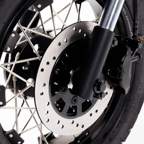 Nahaufnahme eines Coopop Scrambler – 45 km/h Elektroroller & E-Scooter im Scrambler-Design mit 8 kW Spitzenleistung, auf der die Bremsscheibe, der Bremssattel, die Speichen und der Reifen des Vorderrads vor weißem Hintergrund zu sehen sind. Marke: Coopop.