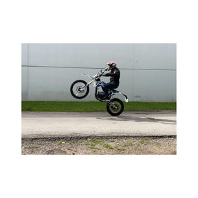 Eine Person in Motorradbekleidung führt auf einem asphaltierten Weg einen Wheelie auf einem TRINITY Panthera II: E-Enduro – einem 125 km/h schnellen Elektro-Enduro-Motorrad mit 4 Gängen – durch.