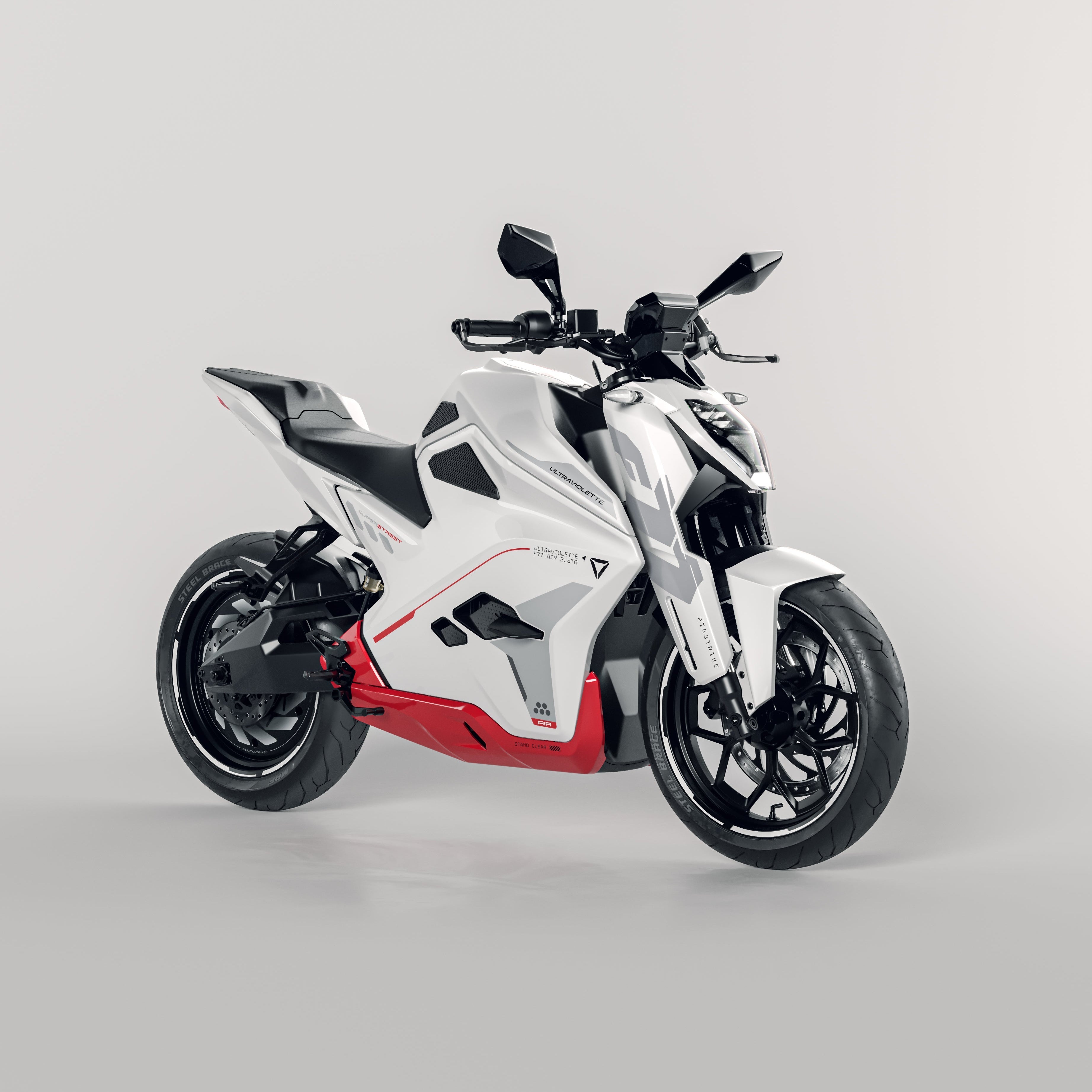 Die Ultraviolette F77 Superstreet Recon, ein schnittiges, weiß-rotes, sportliches Elektromotorrad von Ultraviolette, zeichnet sich durch ein kantiges Design mit schwarzen Akzenten und Seitenspiegeln aus, das sich vor einem schlichten, hellen Hintergrund präsentiert.