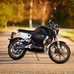 Ein VMOTO TC 72V Elektroroller im Café-Racer-Design mit 45 km/h steht auf einer sonnenbeschienenen Straße, umgeben von verschwommenem Grün und Bäumen im Hintergrund.