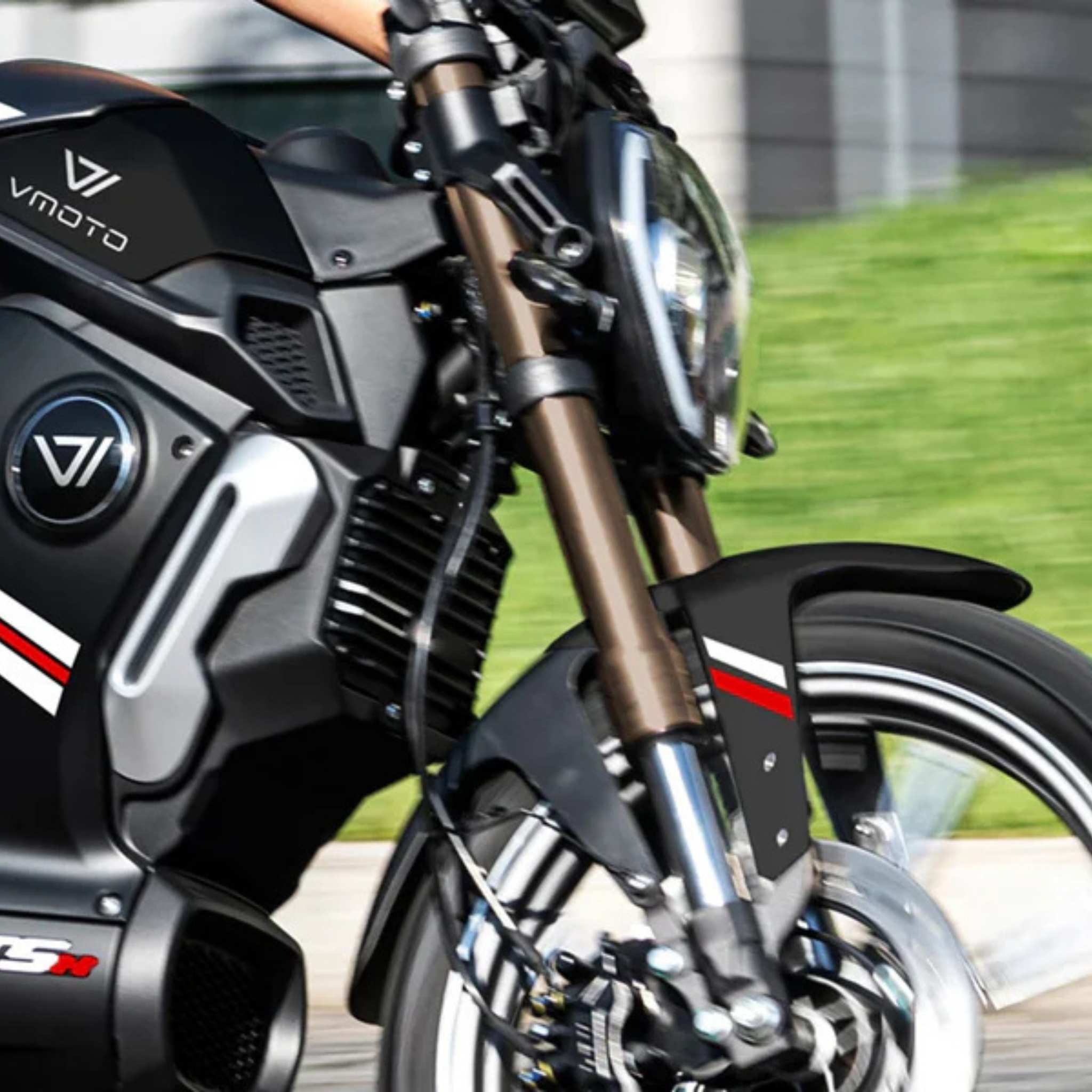 Nahaufnahme des VMOTO TSX 72V, eines leistungsstarken 45 km/h Elektrorollers im Motorrad-Design, in Bewegung. Das schwarz-graue Design mit rot-weißen Akzenten hebt das Vorderrad, die Federung, den Scheinwerfer und einen Teil des Armes des Fahrers hervor. Marke: VMOTO.